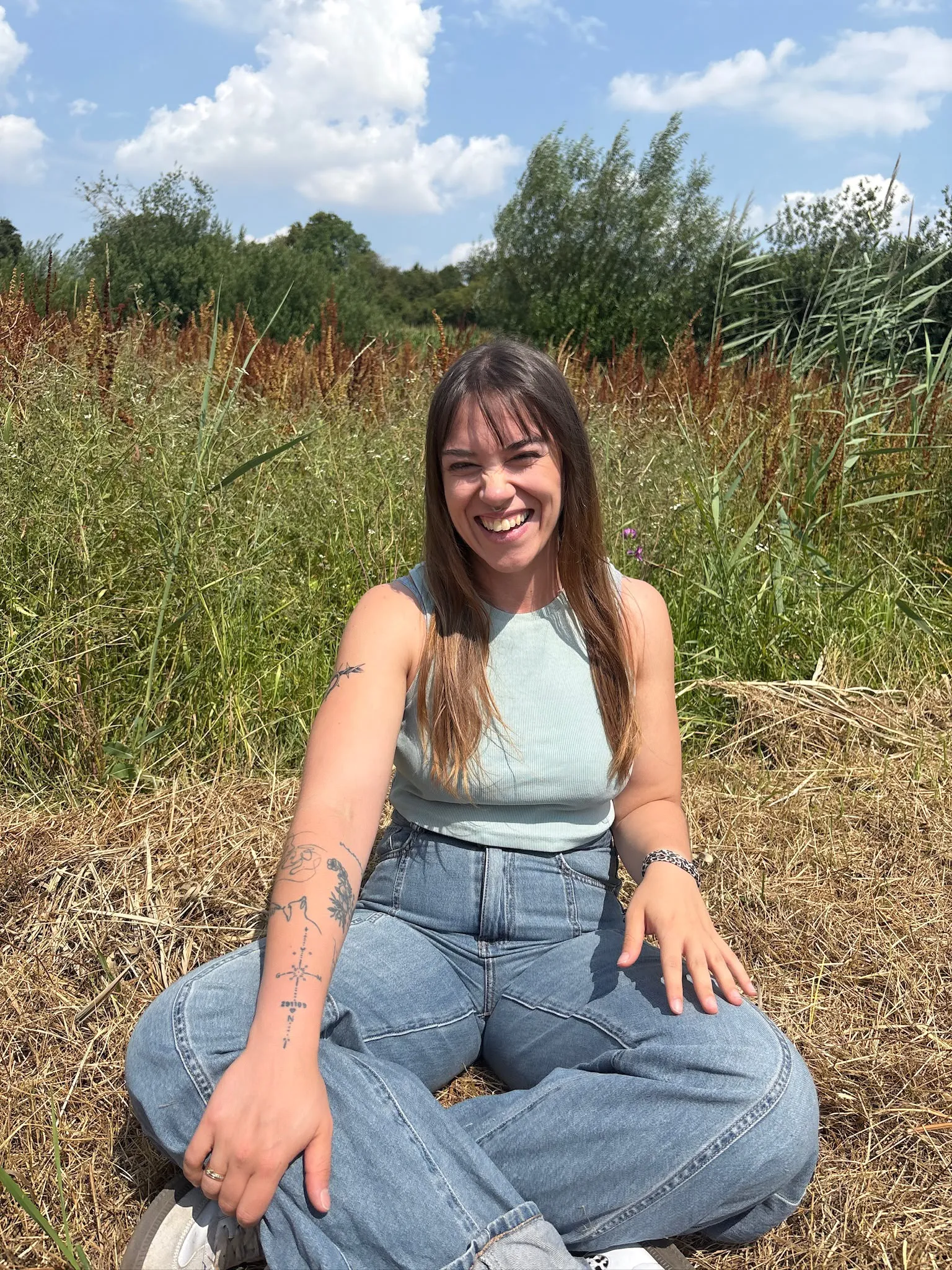 Sarah Bove sitzt lachend auf einer sommerlichen Wiese
